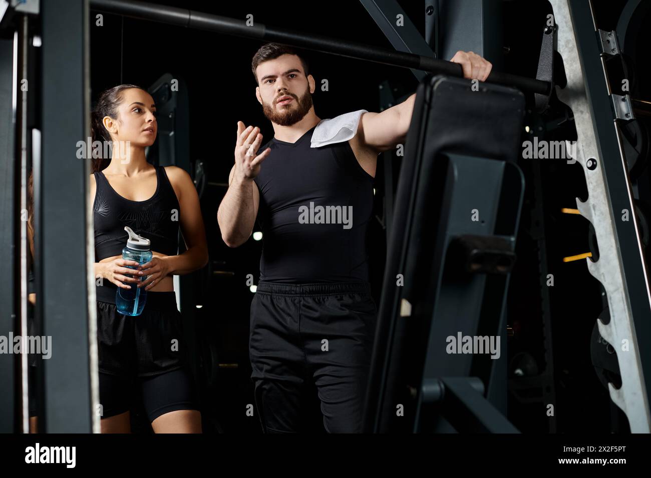 A male personal trainer stands next to a brunette sportswoman in a gym, motivating and guiding her through a workout session. Stock Photo