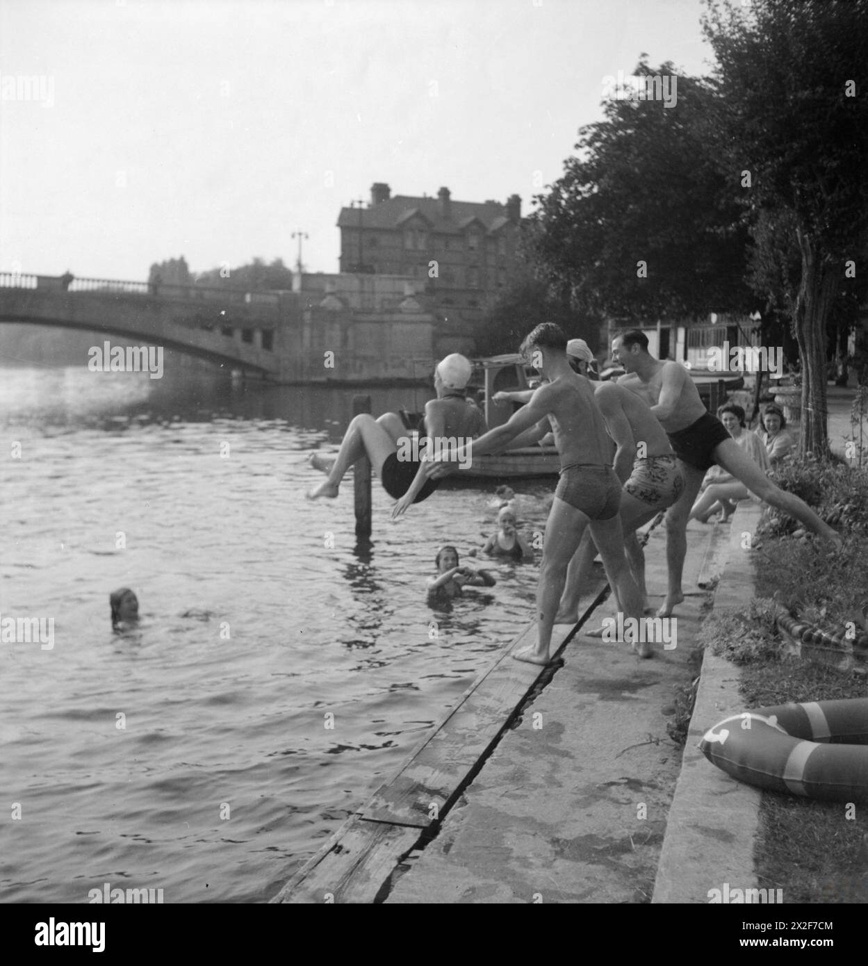 A PICTURE OF A SOUTHERN TOWN: LIFE IN WARTIME READING, BERKSHIRE, ENGLAND, UK, 1945 - A group of young boys throw their female friend into the water as they bathe at the Lido by Caversham Bridge, Reading. Several other people can be seen in the water, enjoying the sunshine Stock Photo