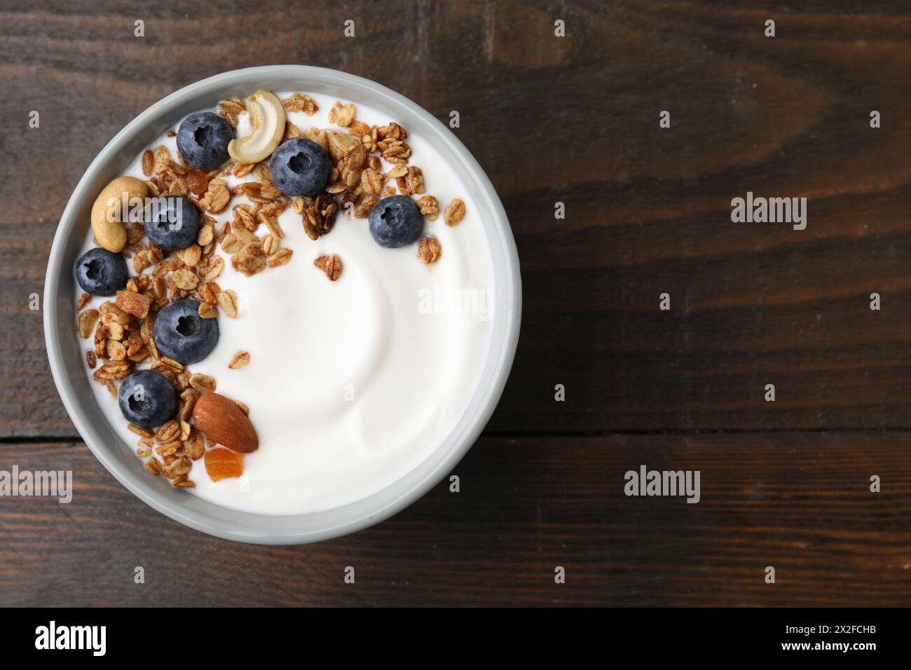 Bowl with yogurt, blueberries and granola on wooden table, top view. Space for text Stock Photo