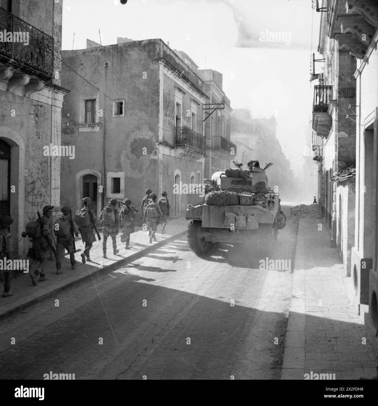 THE BRITISH ARMY IN SICILY 1943 - A Sherman tank and infantry advance through the town of Carlentini, 15 July 1943 Stock Photo