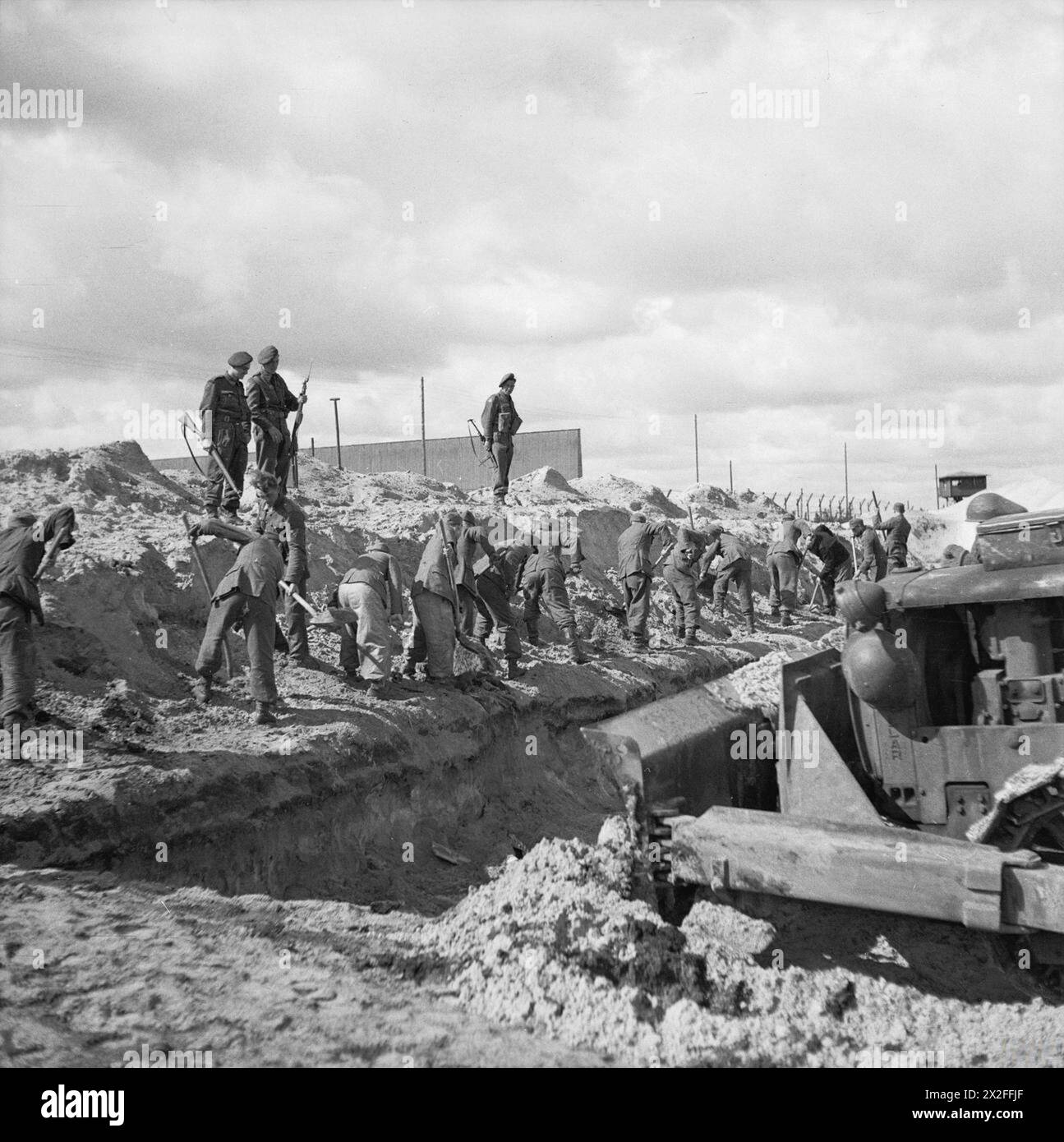 THE LIBERATION OF BERGEN-BELSEN CONCENTRATION CAMP, APRIL 1945 - German SS guards and a bulldozer fill in a mass grave Stock Photo