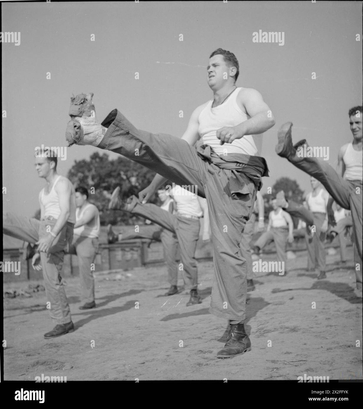 FIRST US ARMY REHABILITATION CENTRE: RECUPERATION AND TRAINING AT 8TH CONVALESCENT HOSPITAL, STONELEIGH PARK, KENILWORTH, WARWICKSHIRE, UK, 1943 - Sergeant M M 'Big Momma' Swindele kicks his leg into the air during an early morning Physical Training session on the parade ground of 8th Convalescent Hospital, Stoneleigh Park. Sergeant Swindele is originally from Oakman, Alabama and fractured his ankle, which is clearly heavily bandaged, in the British blackout. He is in the lowest grade of trainees, grade D, which means that he has quite a way to go before he reaches grade A and full fitness. Ac Stock Photo