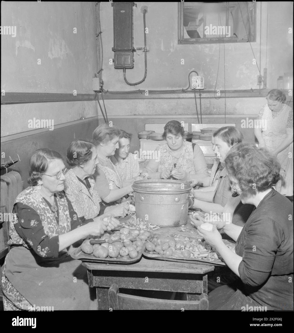 WOOLMORE STREET RESTAURANT: EATING OUT IN WARTIME LONDON, 1942 - Women at work preparing vegetables in the kitchen of the British Restaurant at Woolmore Street. Left to right they are: Mrs F Malyon (aged 59), Mrs C Pude (aged 64, a cigar worker in peacetime), Mrs Florence Skinner, Mrs Davison (once demonstrated cleaning materials), Mrs J Harrop (ran a corn chandler and grocer's store), Doris Prigge (previously in the catering trade), Miss Barkwith, Miss Violet Hancock and Mrs Turley. Another woman can be seen in the background Stock Photo