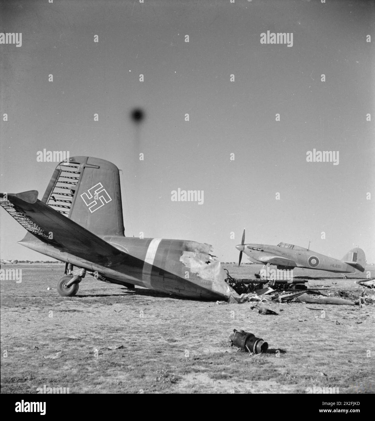 ROYAL AIR FORCE: OPERATIONS IN THE MIDDLE EAST AND NORTH AFRICA, 1939-1943. - Behind the wreckage of a burnt-out Focke Wulf FW 200 Condor, Hawker Hurricane Mark IIB, HL681 'A', of No. 274 Squadron RAF, stands on the landing ground at Castel Benito, Tripolitania, after its capture. 274 Squadron were temporarily installed there until the airfield at Mellaha could be made serviceable for use Royal Air Force, Maintenance Unit, 274 Stock Photo