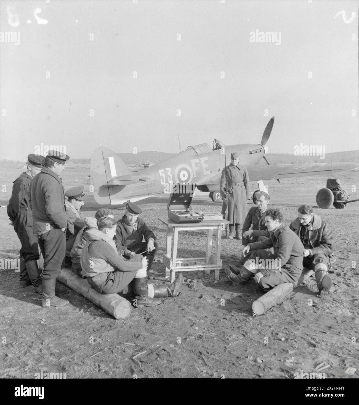 RAF personnel and Soviet sailors gather around a gramophone at a dispersal site in Vaenga while a Russian sentry guards Hawker Hurricane Mark IIB Z5227 'FE-53' of No. 81 Squadron RAF between September and November 1941. Stock Photo