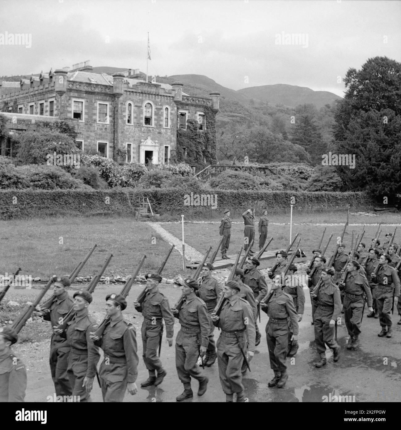 THE FREE FRENCH ARMY IN THE UNITED KINGDOM 1939-1945 - French commando troops undergoing training at Achnacarry House in Scotland: Free French troops, headed by the Commando Depot Pipe Band, march past the Commandant, who is seen taking the salute, with the Free French flag flying from Achnacarry House in the background Free French Army Stock Photo