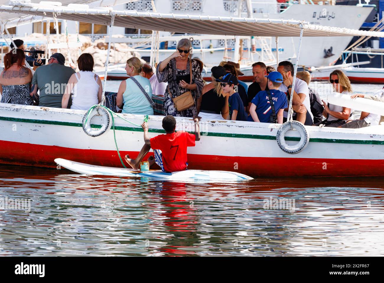 Egyptian boy on a paddleboard, begging from tourists on a Felucca ride. Aswan Harbour, River Nile, Egypt. Stock Photo