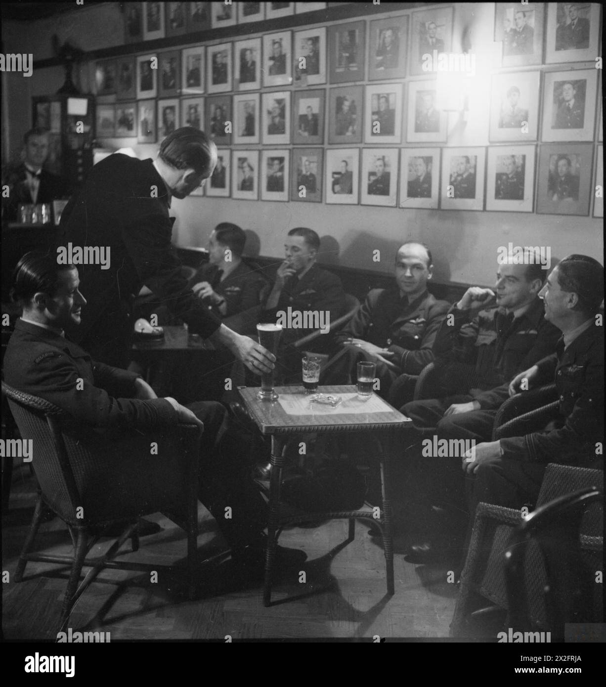 BELGIAN CLUBS AND CAFES IN LONDON: REST, RELAXATION AND ENTERTAINMENT, LONDON, ENGLAND, UK, 1945 - Belgian pilots enjoy a beer, a cigarette and a chat as they relax at 'Aux Neufs Provinces', a club attached to the restaurant 'Chez Gaston', near Victoria Station. The wall behind them is lined with portrait photographs of airmen Stock Photo