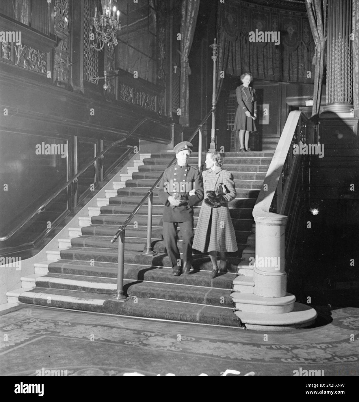CINEMAS AND CINEMA-GOING DURING THE SECOND WORLD WAR - National Fire Service fireman Sydney Chillingworth and his wife Hilda descend the staircase of a cinema, after having seen a film, somewhere in London. An usherette can be seen standing at the top of the stairs Stock Photo