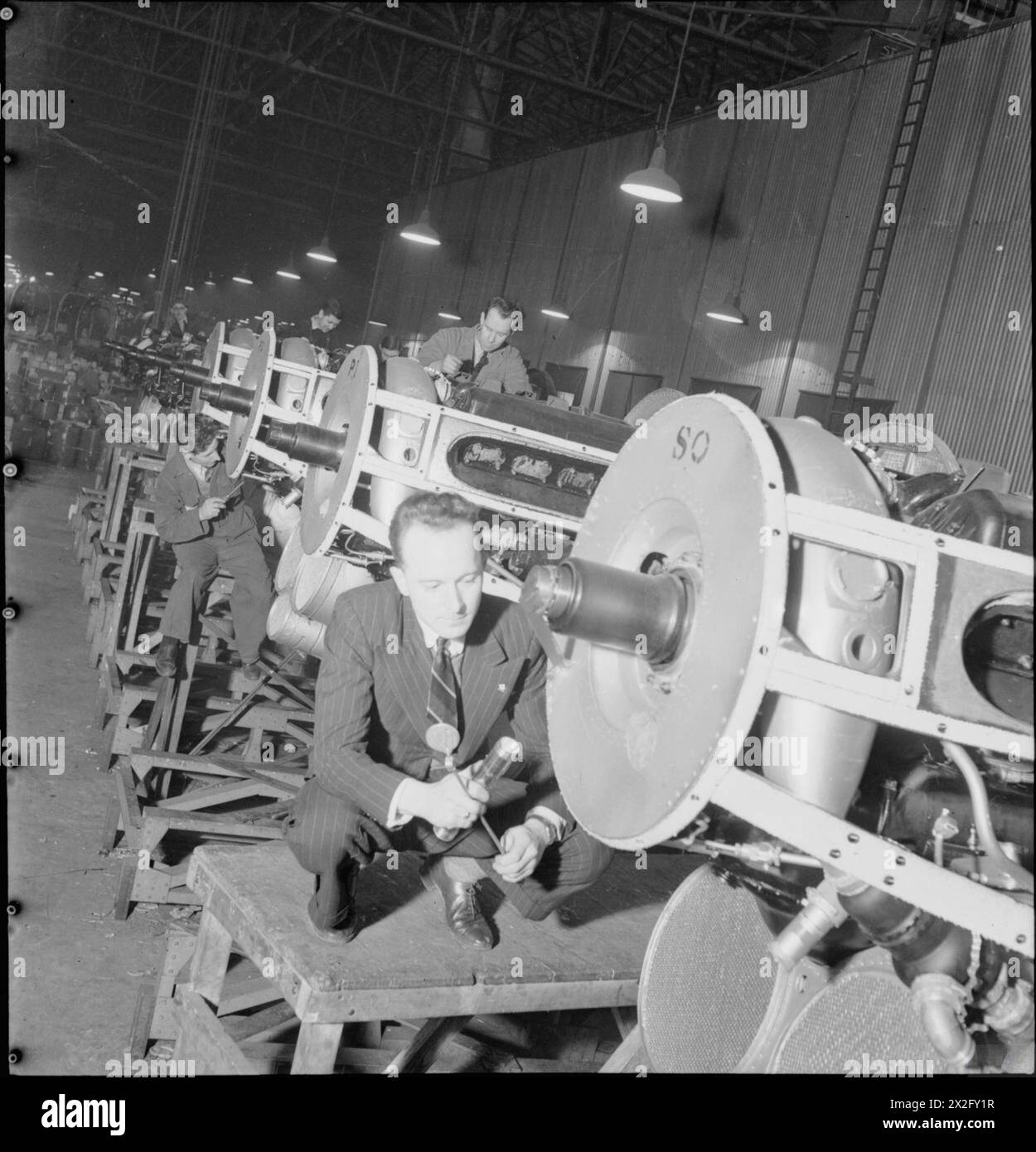 BIRTH OF A BOMBER: AIRCRAFT PRODUCTION IN BRITAIN, 1942 - Men at work on a row of the propeller-end sections of engines for a Halifax bomber at the Handley Page factory in Cricklewood. The propellers themselves are not visible in the photograph Stock Photo