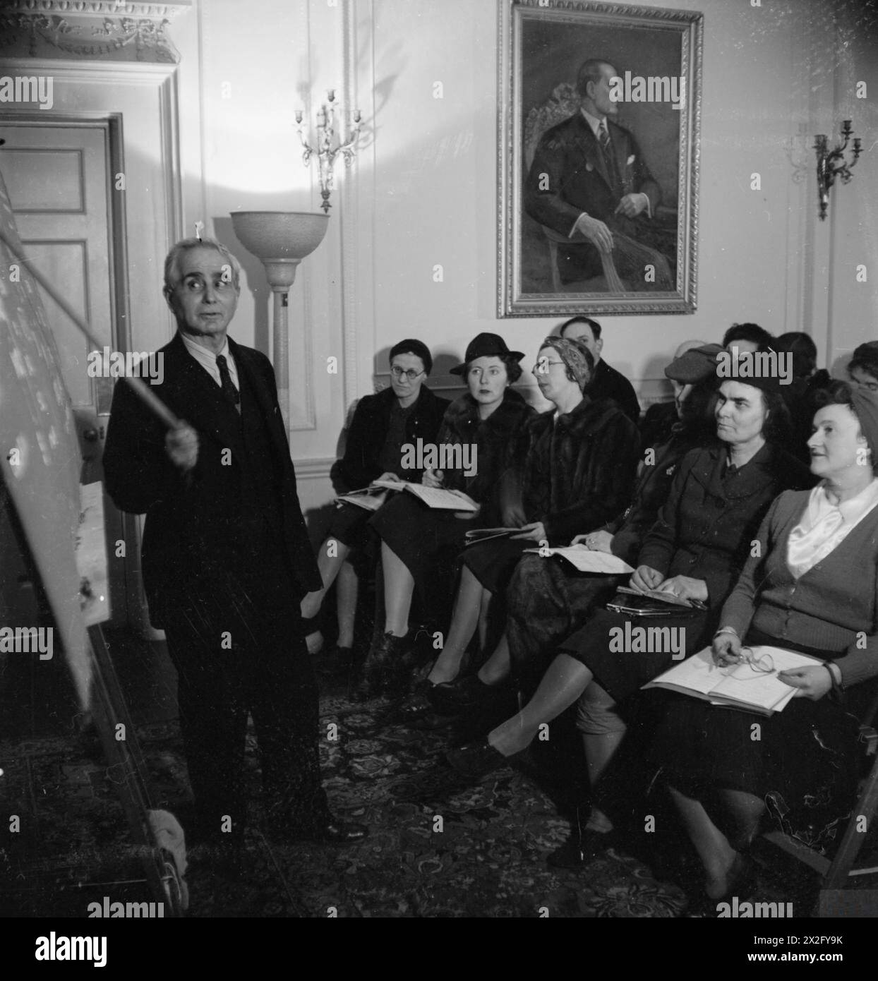 BRITONS LEARN TURKISH: ADULT EDUCATION IN LONDON, 1943 - Bay Ali Riza Sencan, Secretary of the Halkevi, points to the blackboard whilst teaching the class about the three different personal pronoun suffixes. The front row of the class listens intently to him. A portrait of Kemal Ataturk can be seen on the wall behind them. Turkish language classes are held here twice a week Stock Photo