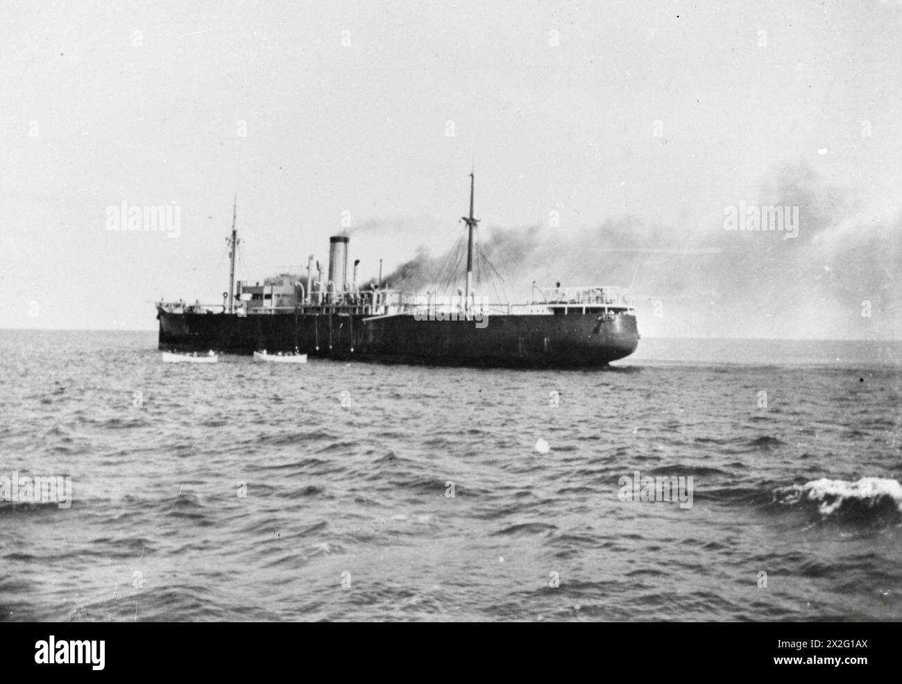 THE INTERCEPTION AND SCUTTLING OF THE GERMAN SS IDARWALD. 8 AND 9 DECEMBER 1940, ON BOARD A BRITISH WARSHIP OFF CUBA. THE GERMAN HAMBURG-AMERIKA FREIGHTER IDARWALD WAS INTERCEPTED BY A PATROLLING BRITISH WARSHIP OFF CUBA. THE GERMAN CREW AT ONCE SCUTTLED THEIR SHIP, SET FIRE TO HER, AND TOOK TO THEIR BOATS. THE BRITISH SHIP FOUGHT THE FIRE AND TOOK THE IDARWALD IN TOW, BUT SHE HAD TO BE CAST OFF SHORTLY THEREAFTER AND SANK. - The IDARWALD is well on fire amidships as the boats pull away from the abandoned ship Stock Photo