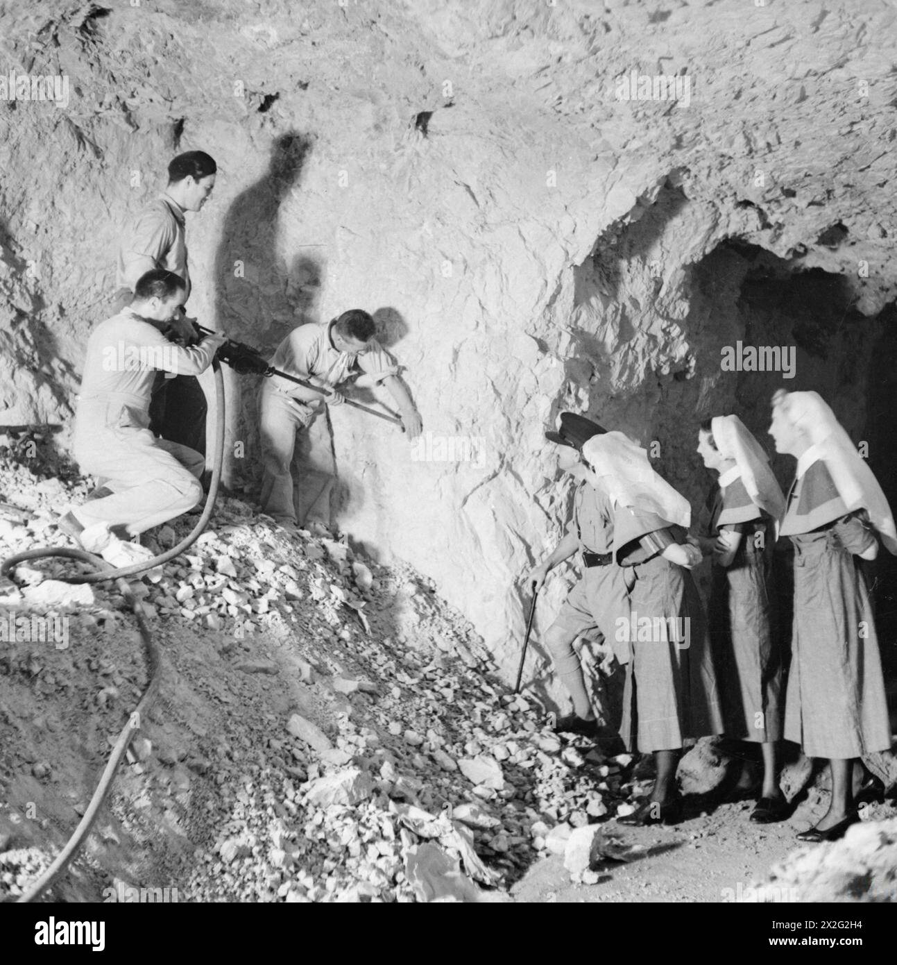 IN A GIBRALTER UNDERGROUND HOSPITAL - When most of the civilian population of Gibralter was evacuated, a hospital was established in one of the air raid shelters cut into the solid rock. It is constantly being added to and is ready for any eventuality. The work of excavation is being done by Civilian engineers, leaving the Royal Engineers to concentrate on defence works. This image shows skilled civilian workmen of the new City Council's staff engaged in construction of a new ward of the hospital. Officer Commanding Hospital and Nursing Staff look on British Army, Royal Engineers Stock Photo