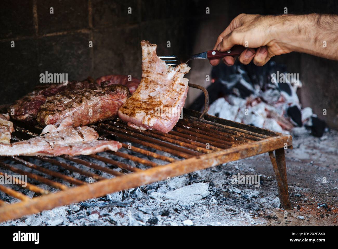 Man cooking the meat on the fire, making the barbecue on the coals in the grill of his house. Traditional Asado of Argentina, Chile, Paraguay y Urugua Stock Photo