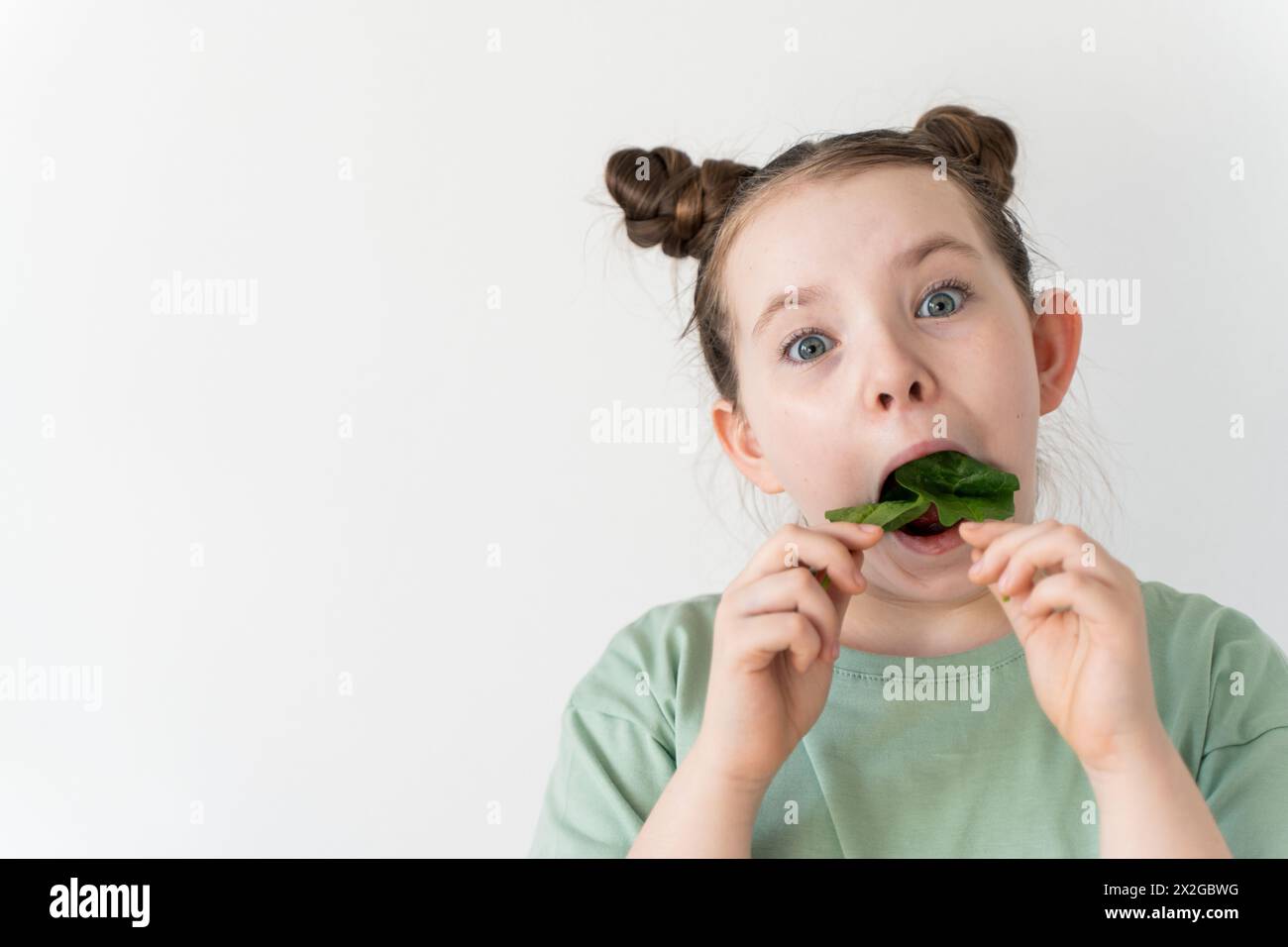 Crazy little girl stuffing spinach leaves into her mouth. Fun, wholesome food. High quality photo Stock Photo