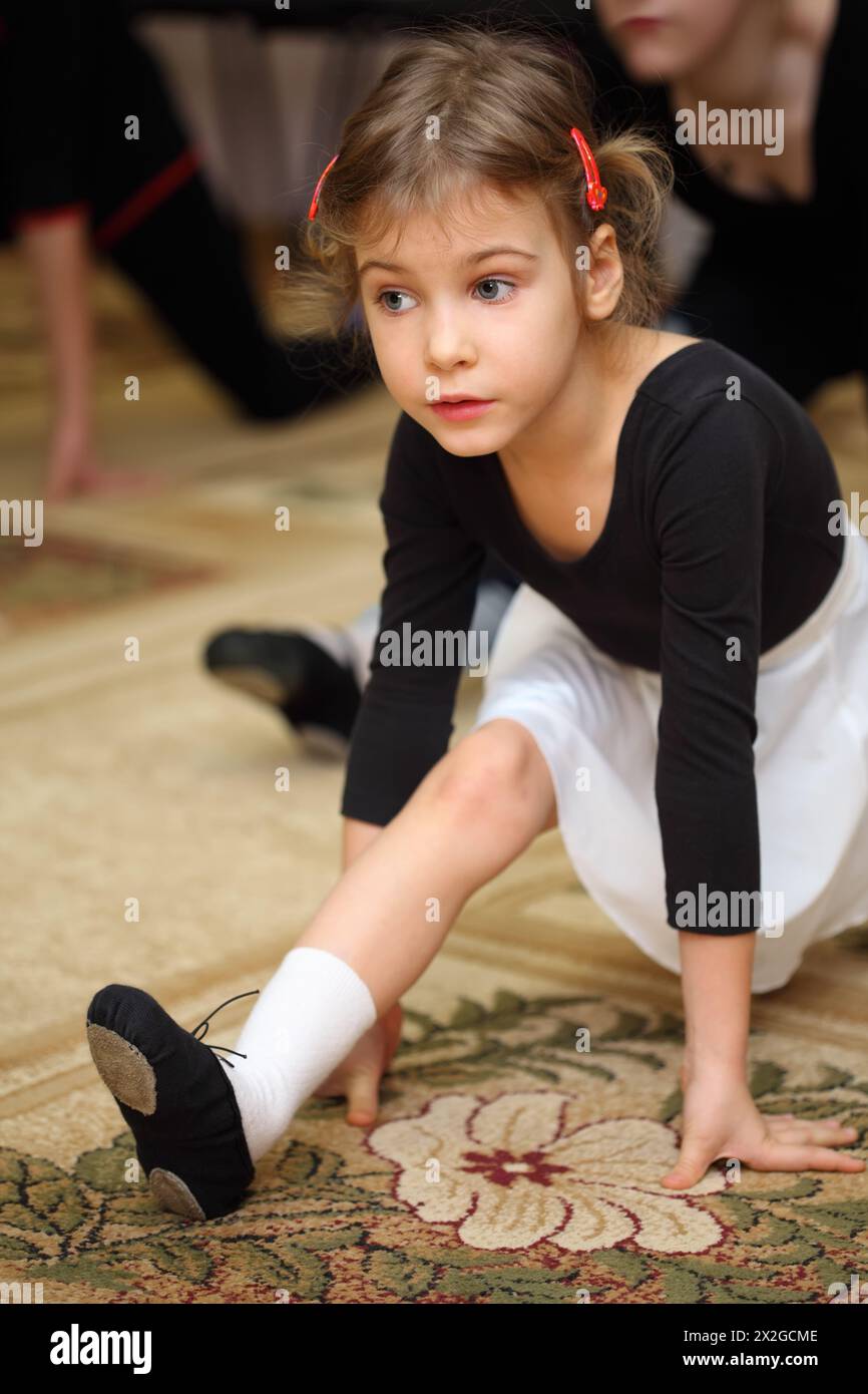 little girl in ballet class sits on string on floor with carpet Stock
