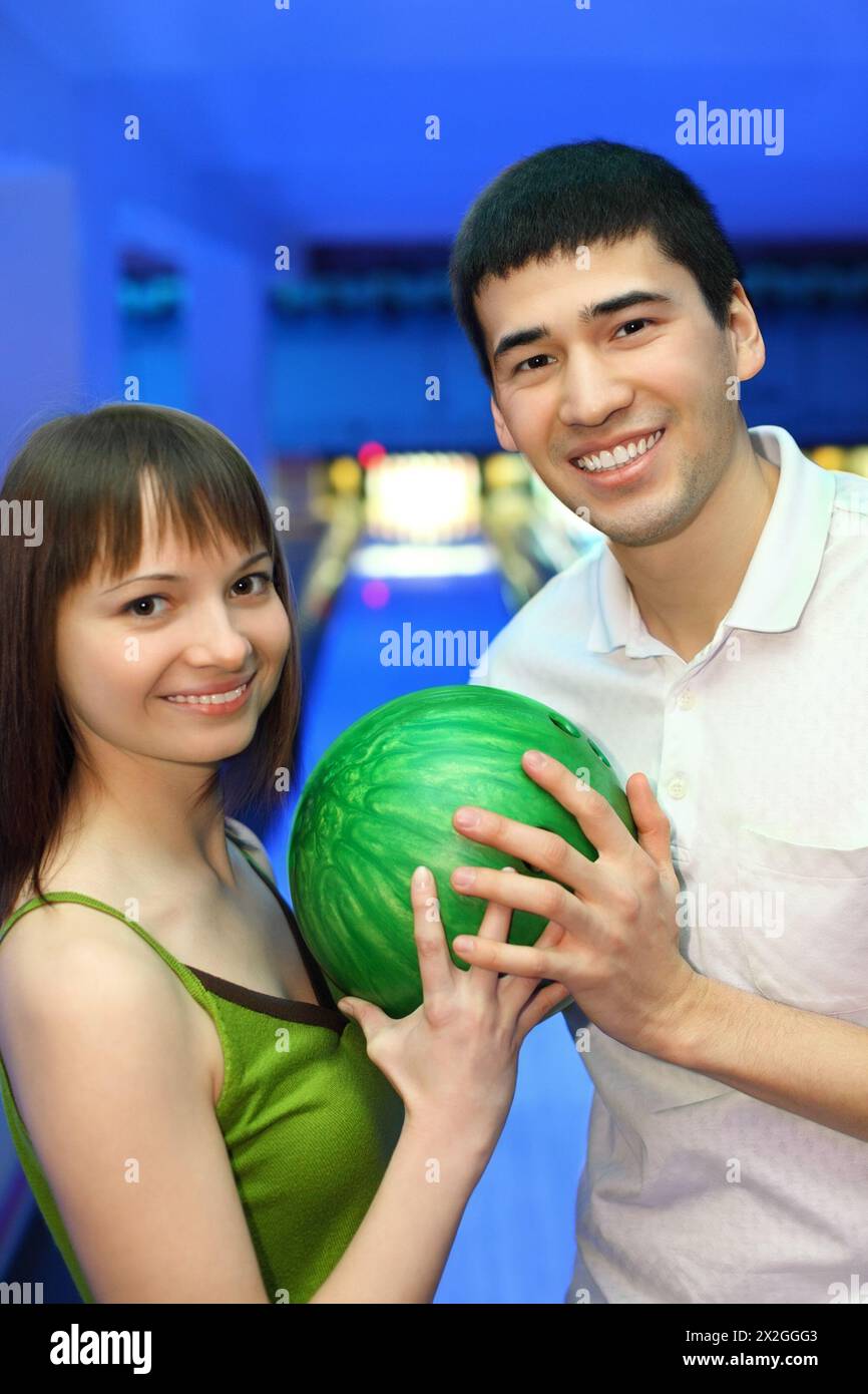Fellow and girl turned to each other and hold one ball for bowling
