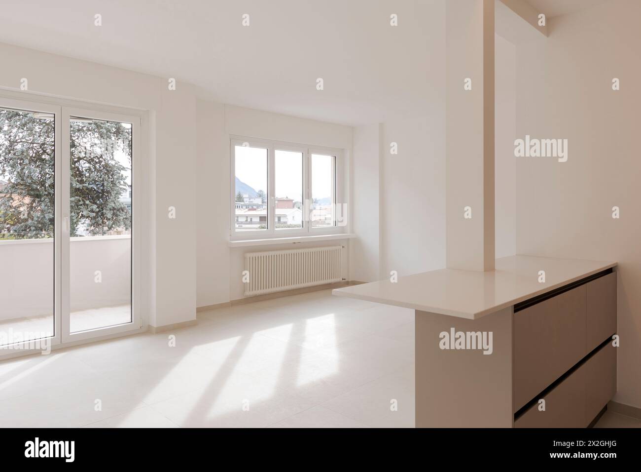 Empty interior of a room, living room of a private flat.  The space is new and in the background two large windows through which light enters Stock Photo