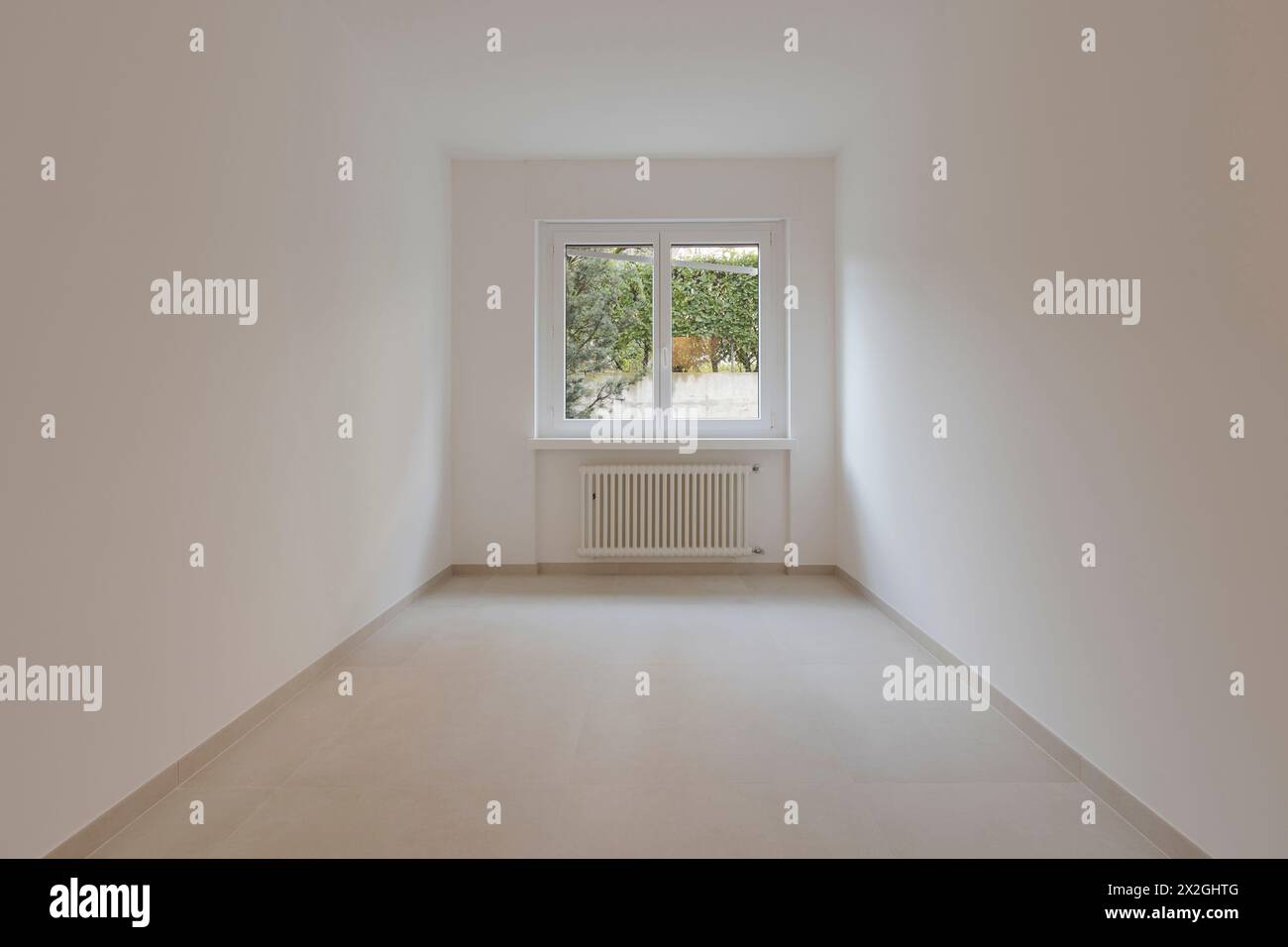 Empty interior of a room, with a central window in the background. Under the window a radiator. Stock Photo