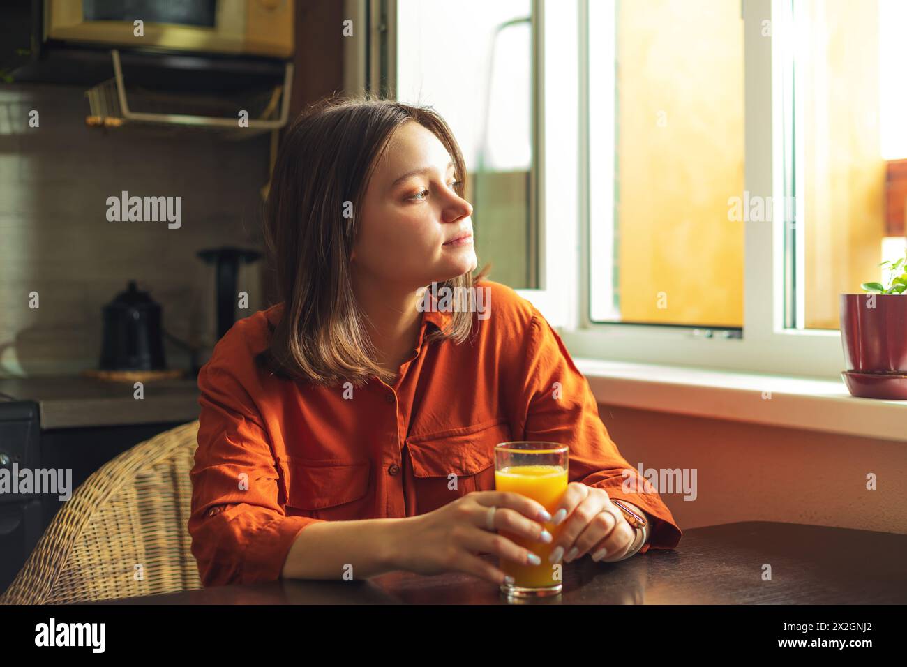 Portrait of a pretty woman with a glass of orange juice. Beautiful young woman sitting in the kitchen at home. Healthy eating concept, detoxification. Stock Photo