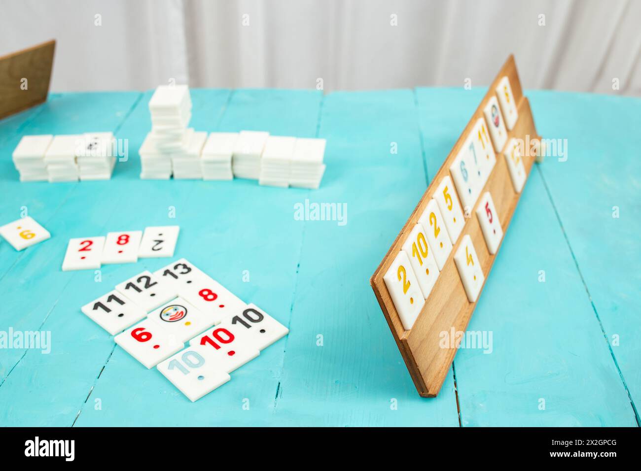 Plastic tiles from the game rummikub, rummicub or  okey in Turkey arranged on a wooden rack, on blue table Stock Photo
