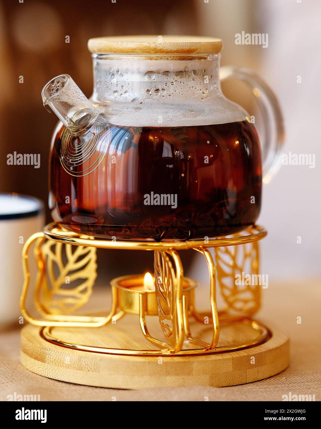 Glass teapot on a stand heated by a candle. Black tea in a glass teapot on the table. Selective focus. Stock Photo