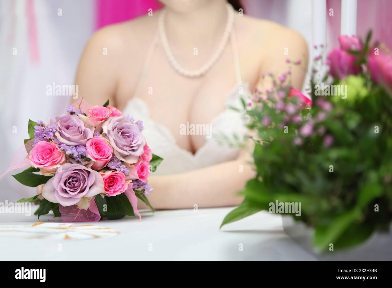 decollete of young bride, which sits at table with candles and holds bouquet of roses; focus on flowers Stock Photo