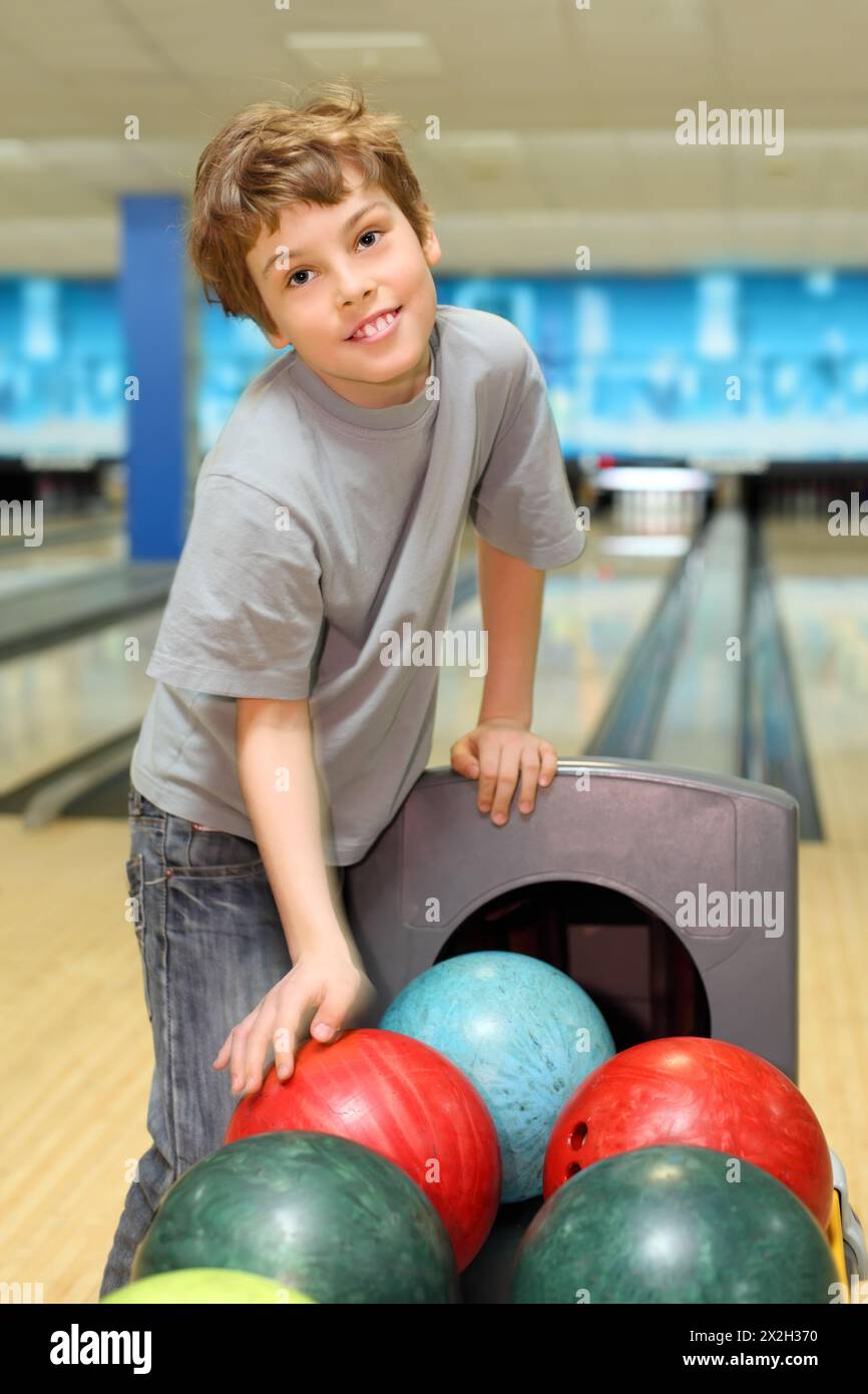 smiling happy boy stands near many colorful balls in bowling club Stock ...