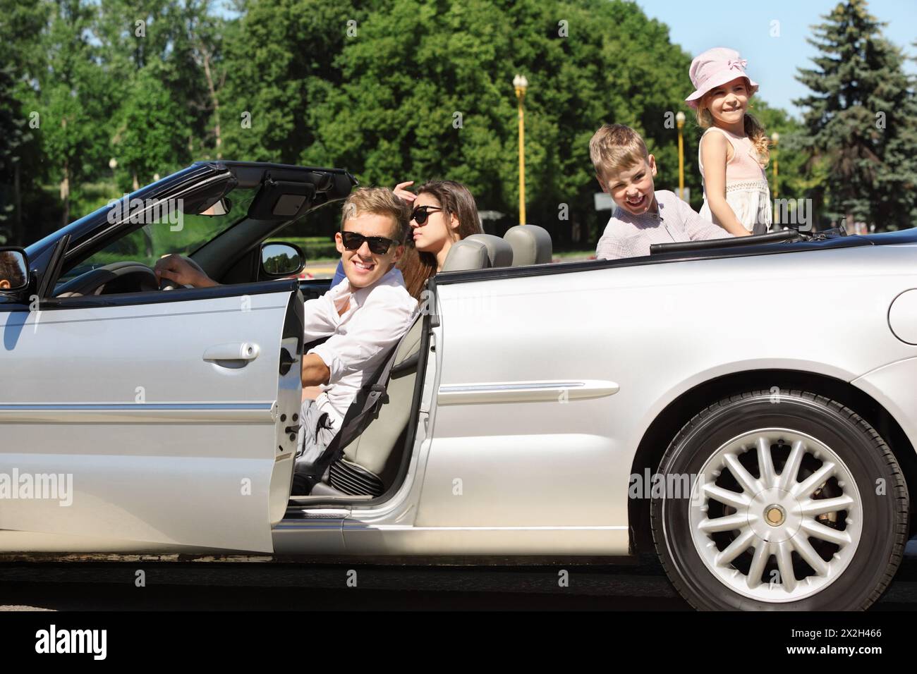 Happy father, mother and two children sit in beautiful convertible car Stock Photo