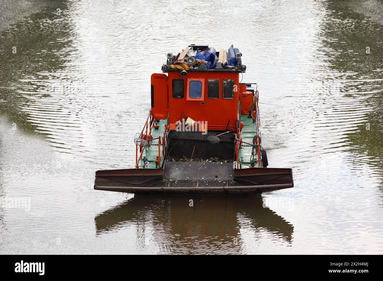 small red boat floats down river and clean river of debris, clean sweep device Stock Photo
