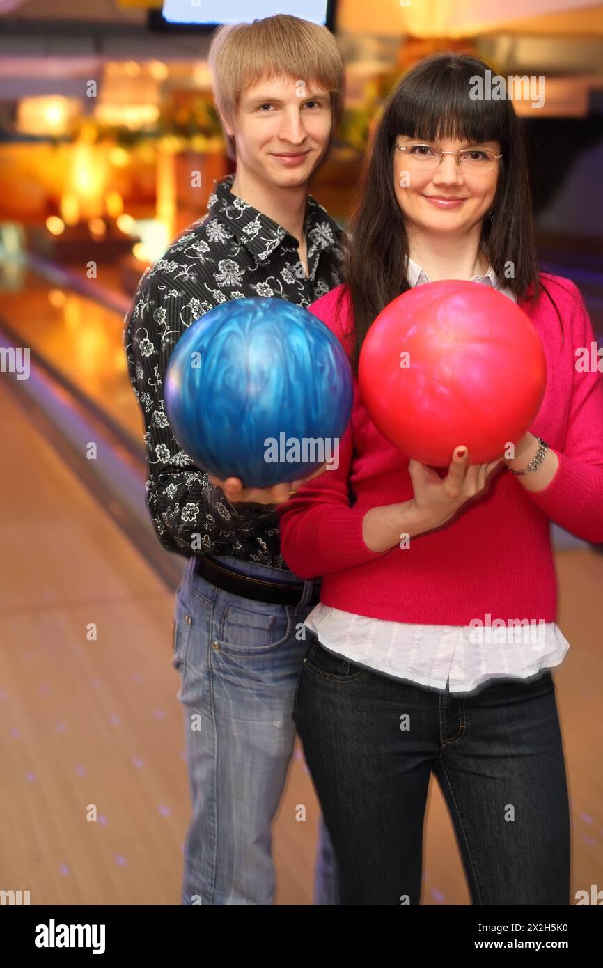 smiling young wife and husband with balls stand in bowling club Stock Photo