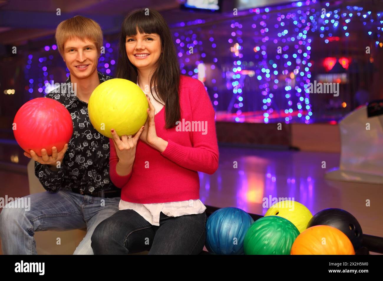 smiling young wife and husband with red and yellow balls sit in bowling club Stock Photo