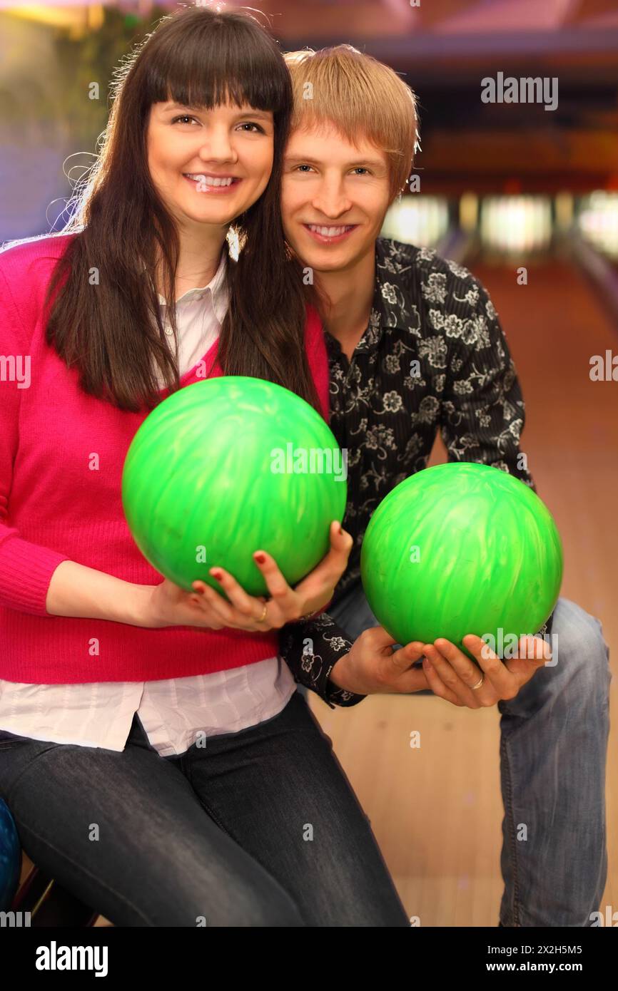 smiling young wife and husband with green balls sit in bowling club Stock Photo