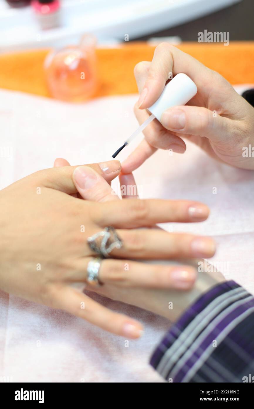Female hands manicure woman by transparent nail polish in beauty salon Stock Photo