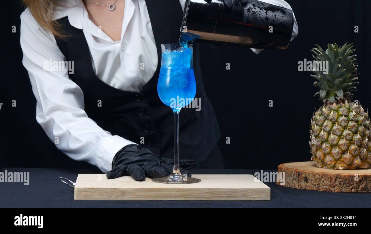 Macrography, experience the artistry of a skilled bartender's hand as they expertly pouring a Blue Hawaii cocktail in glass against a striking black Stock Photo
