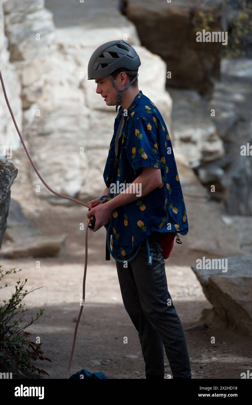 Male climber securing rope to harness prior to belaying another climber ...