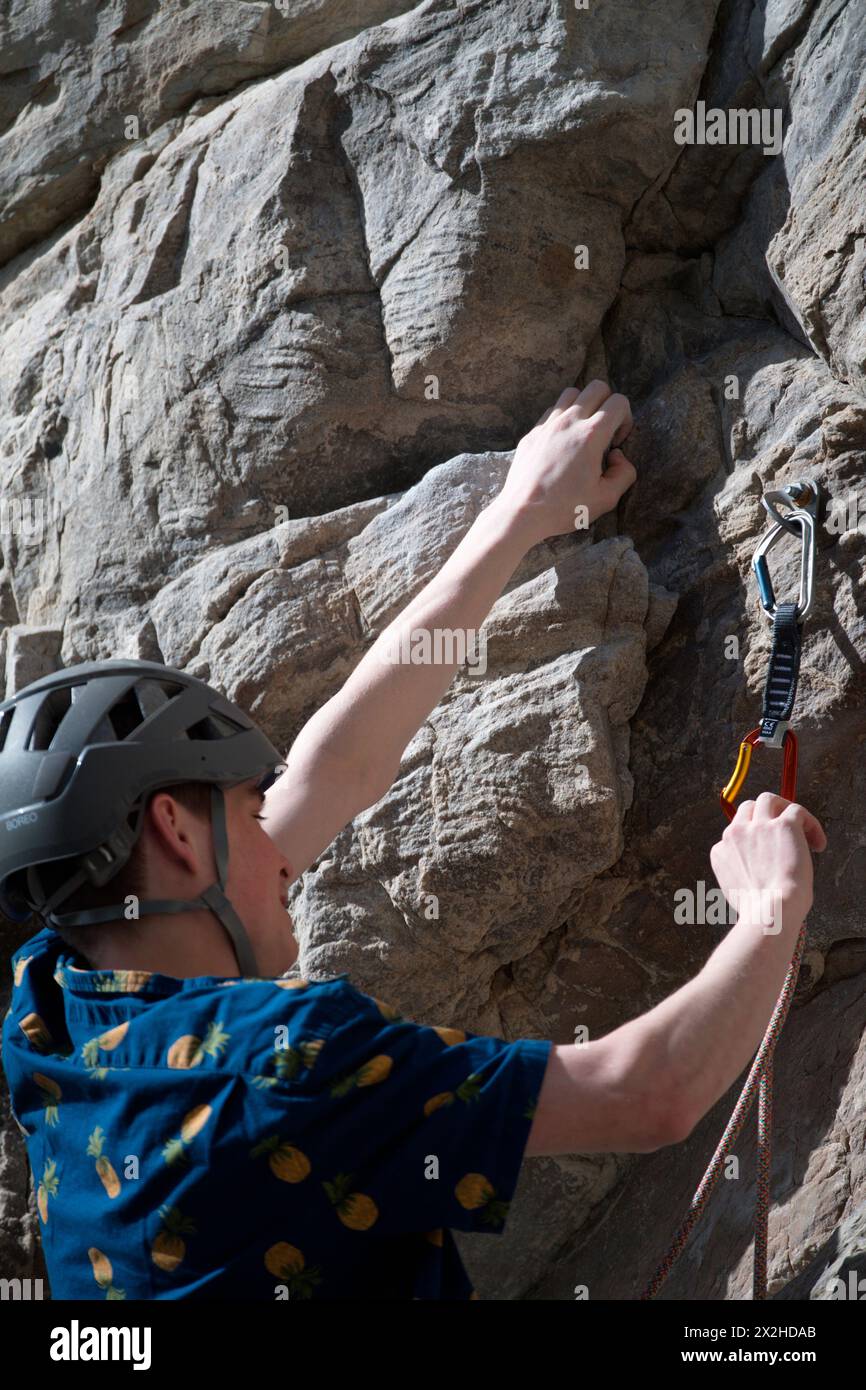 Side view of male climber attaching rope to quick draw on rock face ...