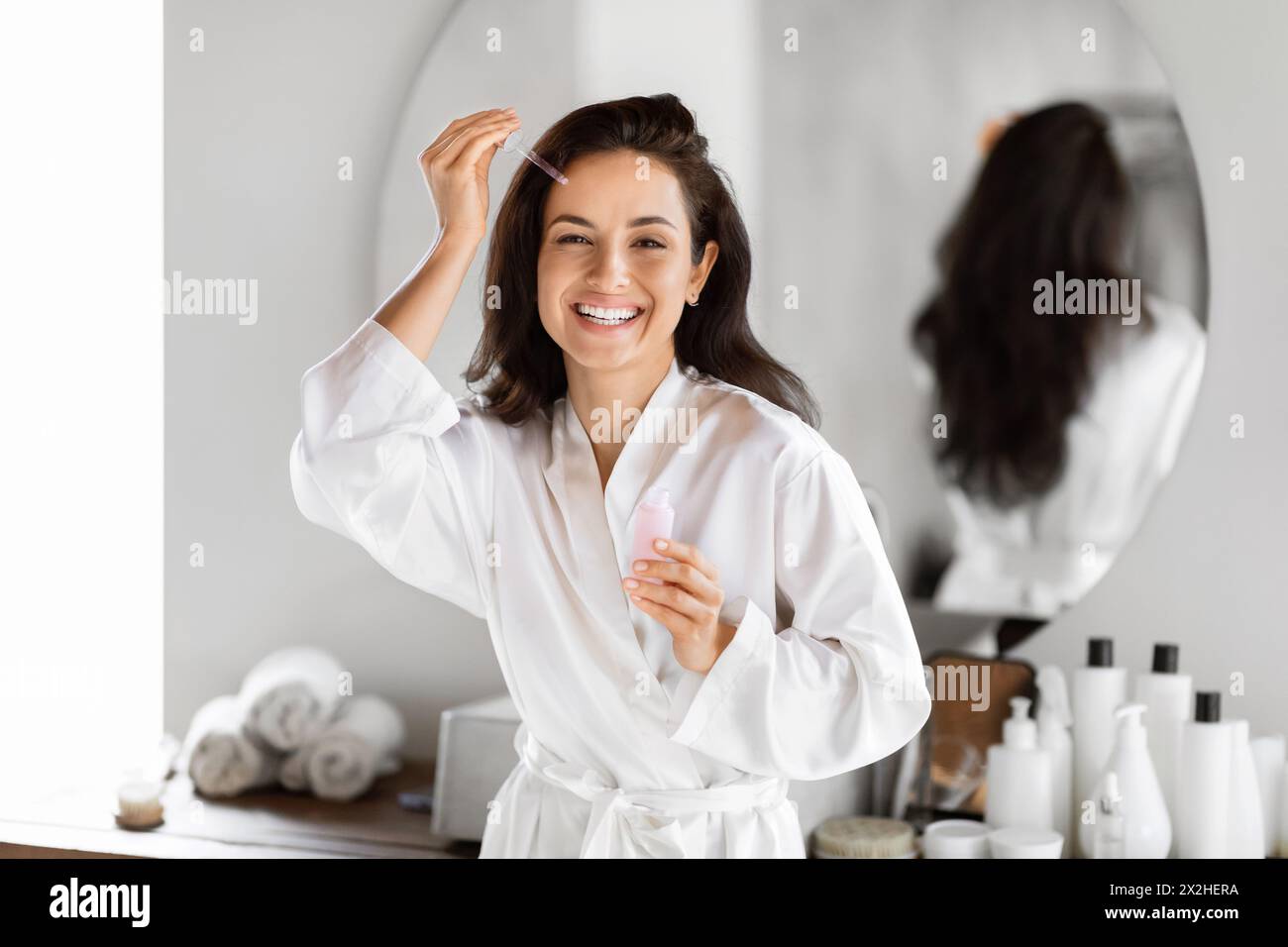 Woman smiling holding skincare product at bathroom Stock Photo