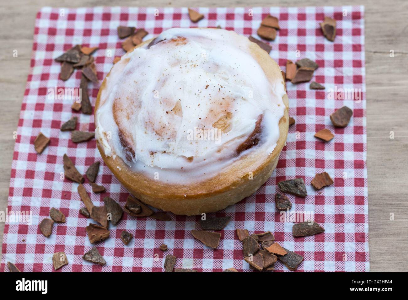 Cinnamon Roll with Frosting on Top, served on red and white napkin with scattered pieces of cinnamon Stock Photo