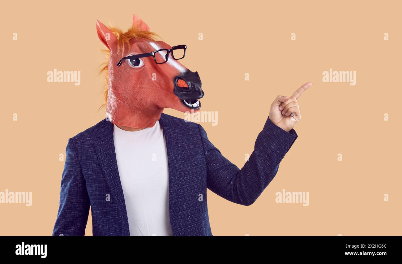 Strange man in a suit, a funny horse mask and glasses pointing his finger to the side Stock Photo
