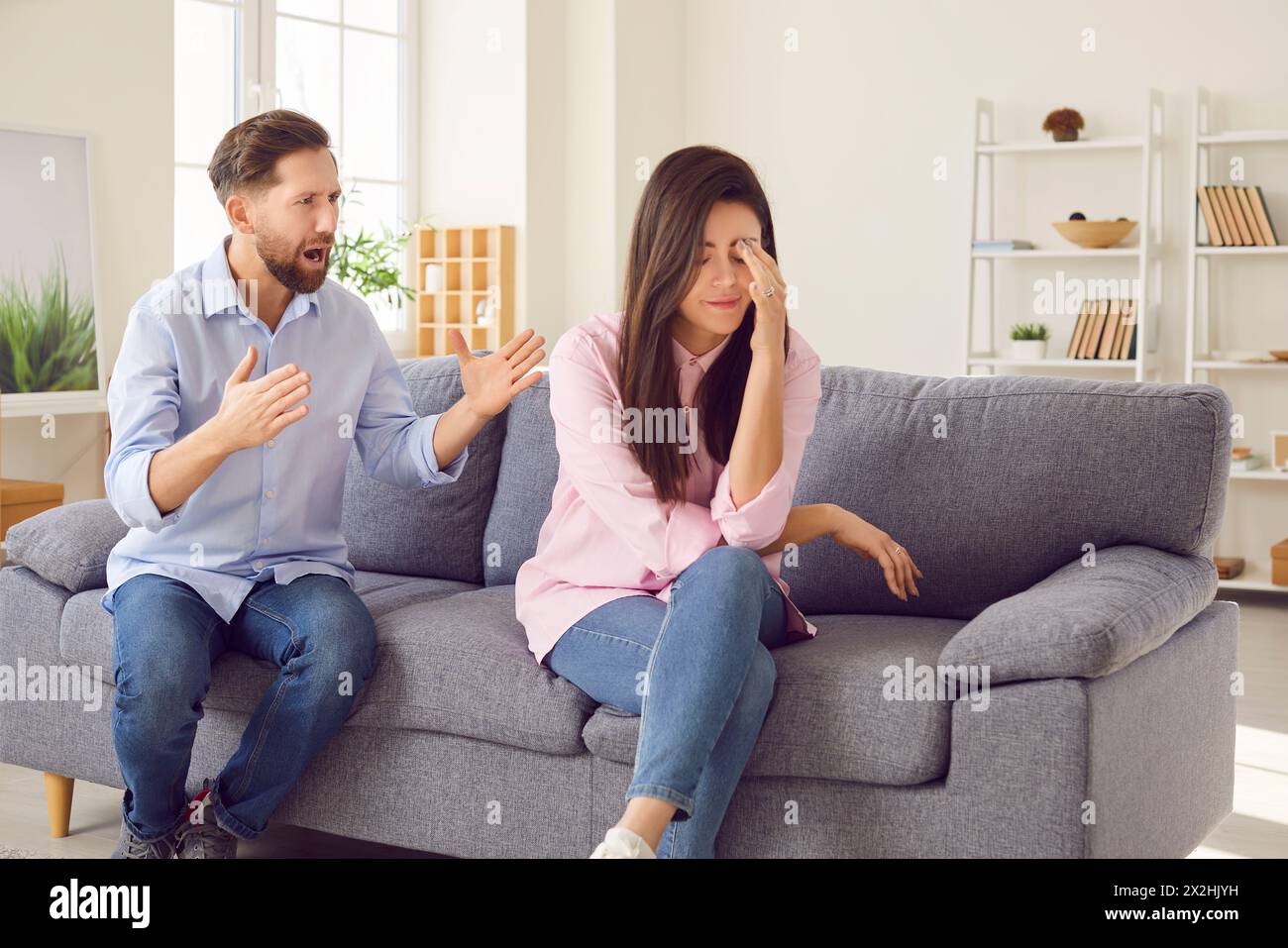 Angry husband shouting in quarrel on his unhappy upset wife sitting on sofa at home Stock Photo