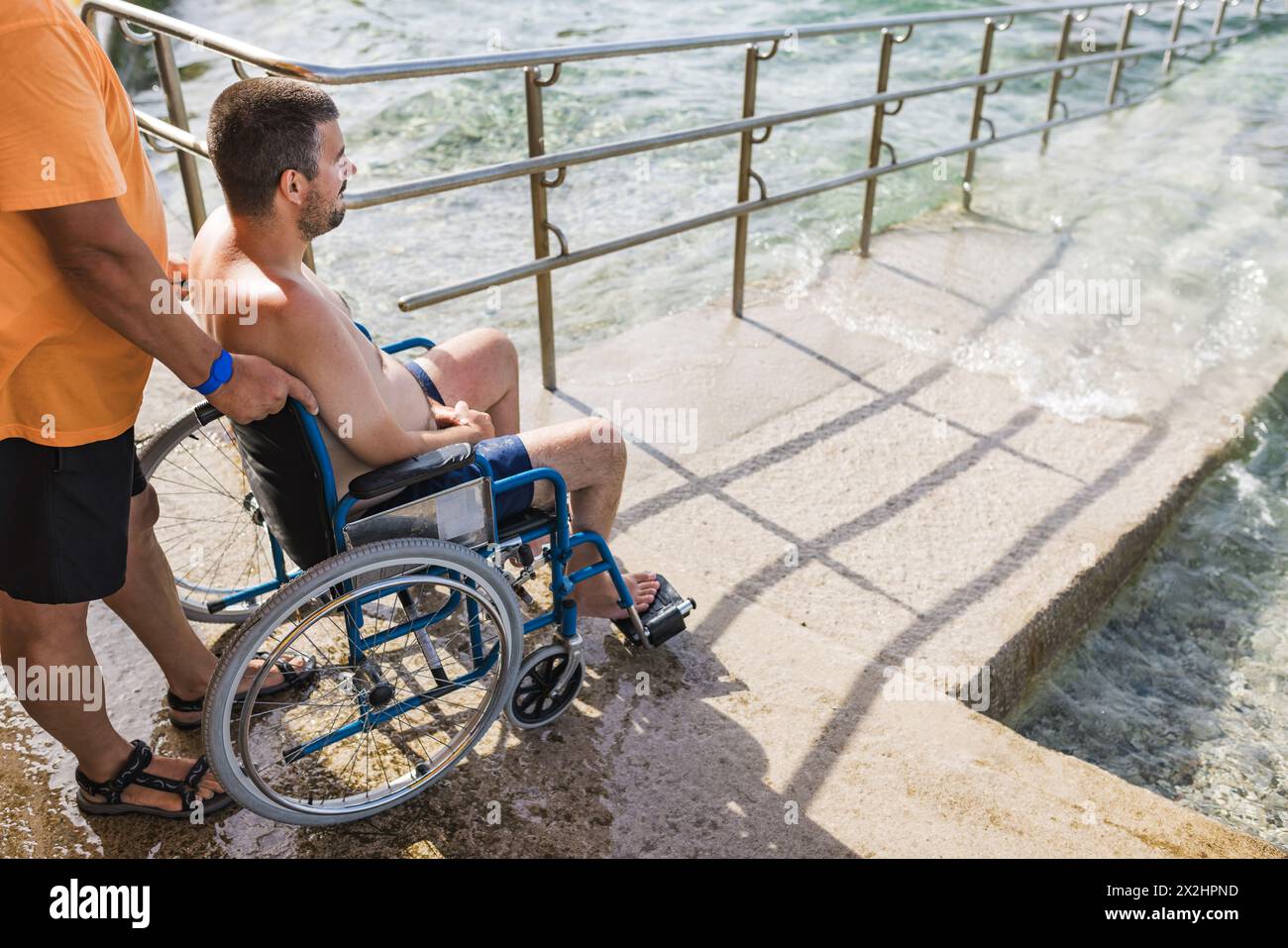 Order Man Ramp Assistant Male assistant helping a man in a wheelchair to enjoy the sea on an ...