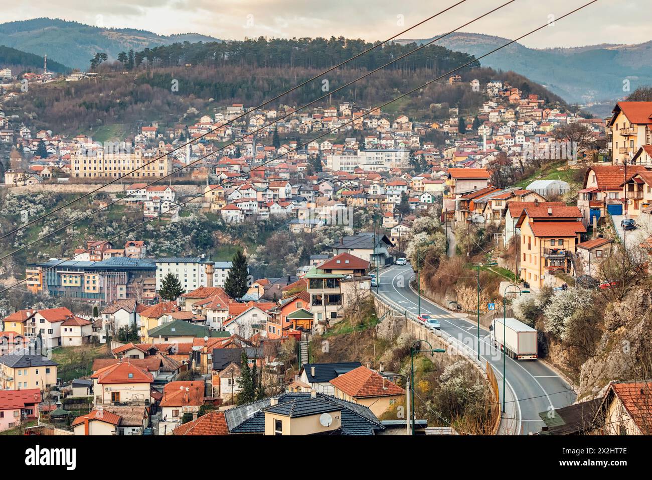 At sunset, Sarajevo's cityscape unfolds, with winding roads weaving through colorful neighborhoods against the backdrop of majestic mountains. Stock Photo