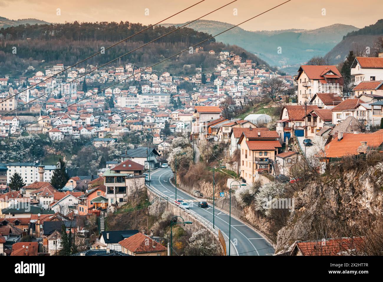 At sunset, Sarajevo's cityscape unfolds, with winding roads weaving through colorful neighborhoods against the backdrop of majestic mountains. Stock Photo