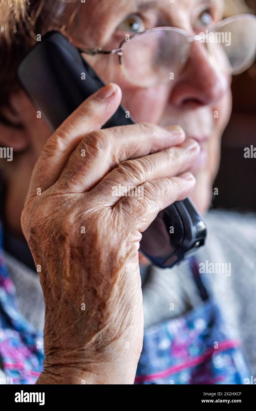 Senior citizen looks serious, frightened while talking on the phone in her living room, Cologne, North Rhine-Westphalia, Germany Stock Photo