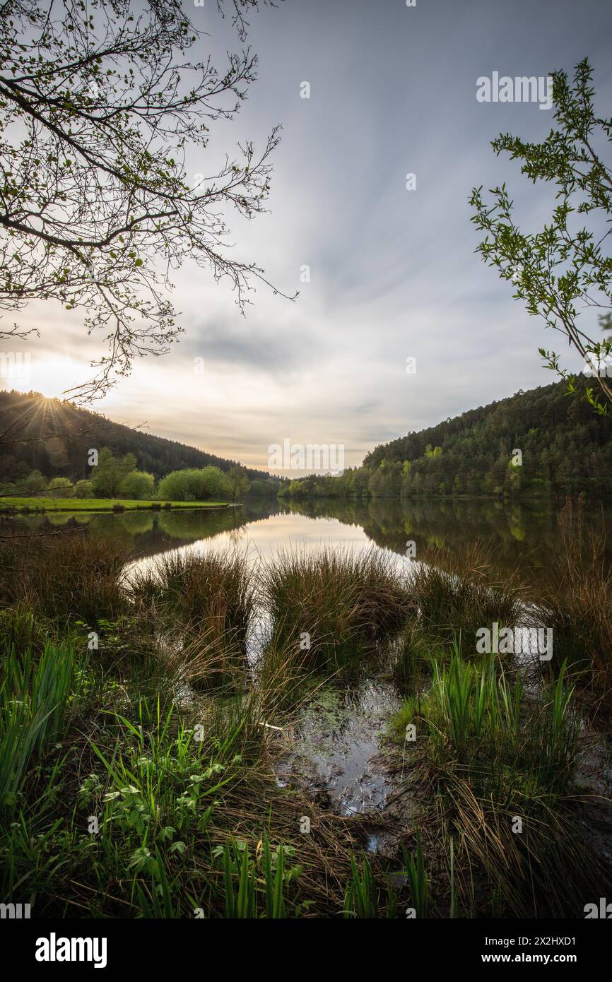 A lake in a landscape shot. A sunset and the natural surroundings are reflected in the water of the reservoir. Marbach reservoir, Odenwald, Hesse Stock Photo