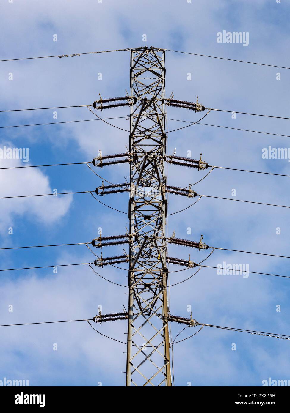 A high-voltage transmission pole with visible wires and insulators against a blue, slightly cloudy sky. Power lines, strategic infrastructure. Stock Photo