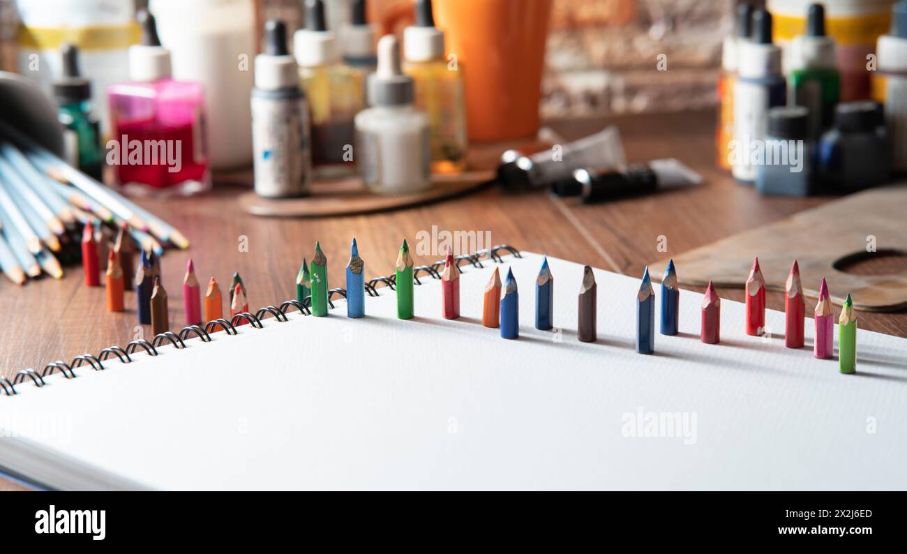 Small colored pencils on white paper on a wooden table with art supplies in the background out of focus Stock Photo