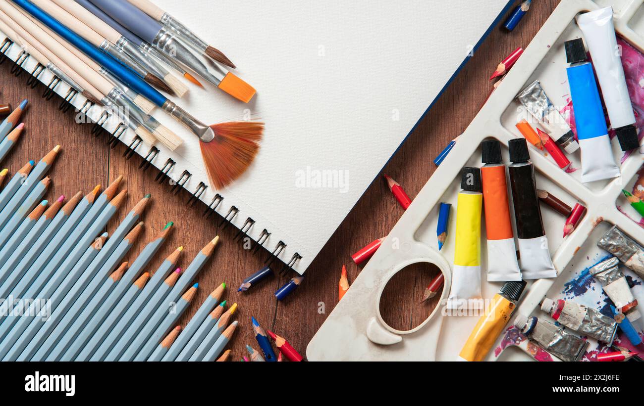Top view of wooden table with pencils, paint tubes, art supplies, variety of brushes on white paper Stock Photo