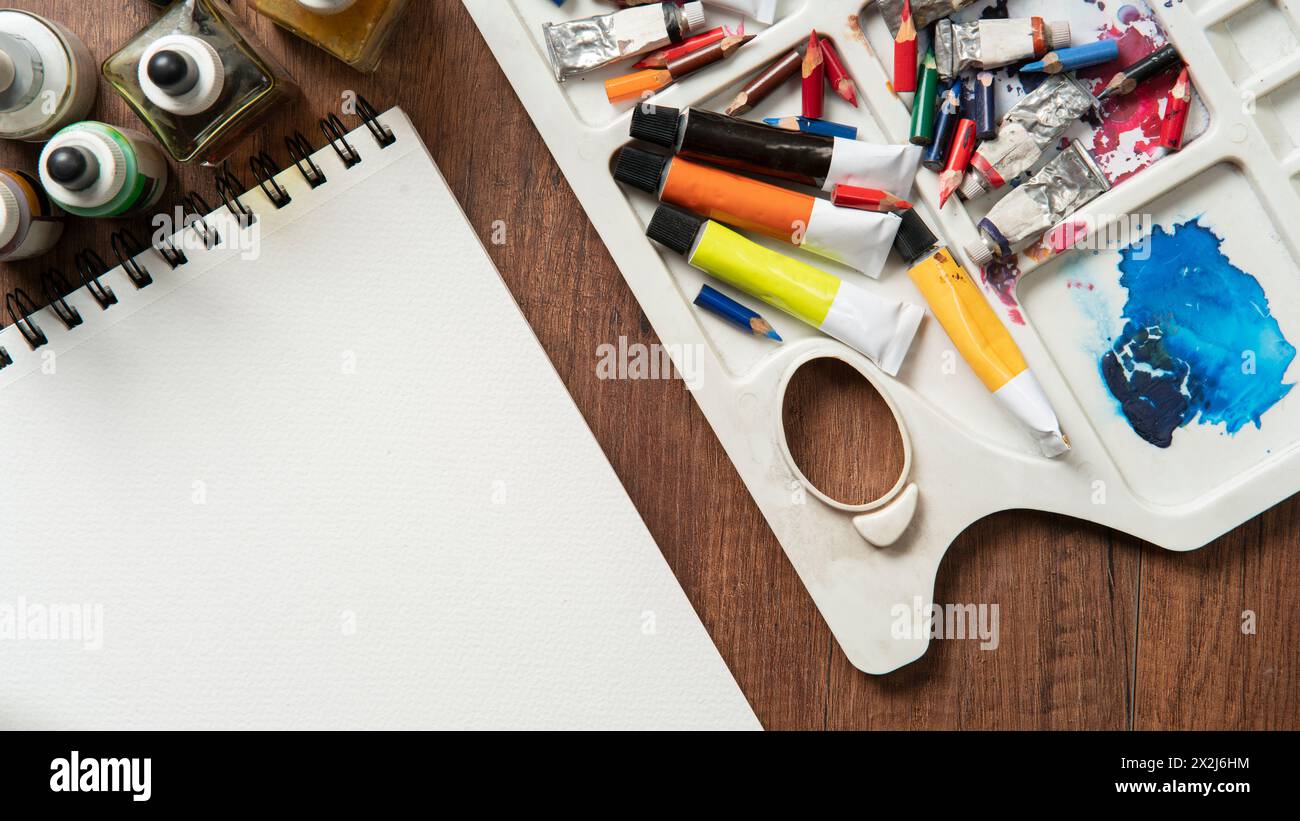 Top view of wooden table with pencils, paint tubes, art supplies, ink bottles, variety of brushes on white paper Stock Photo